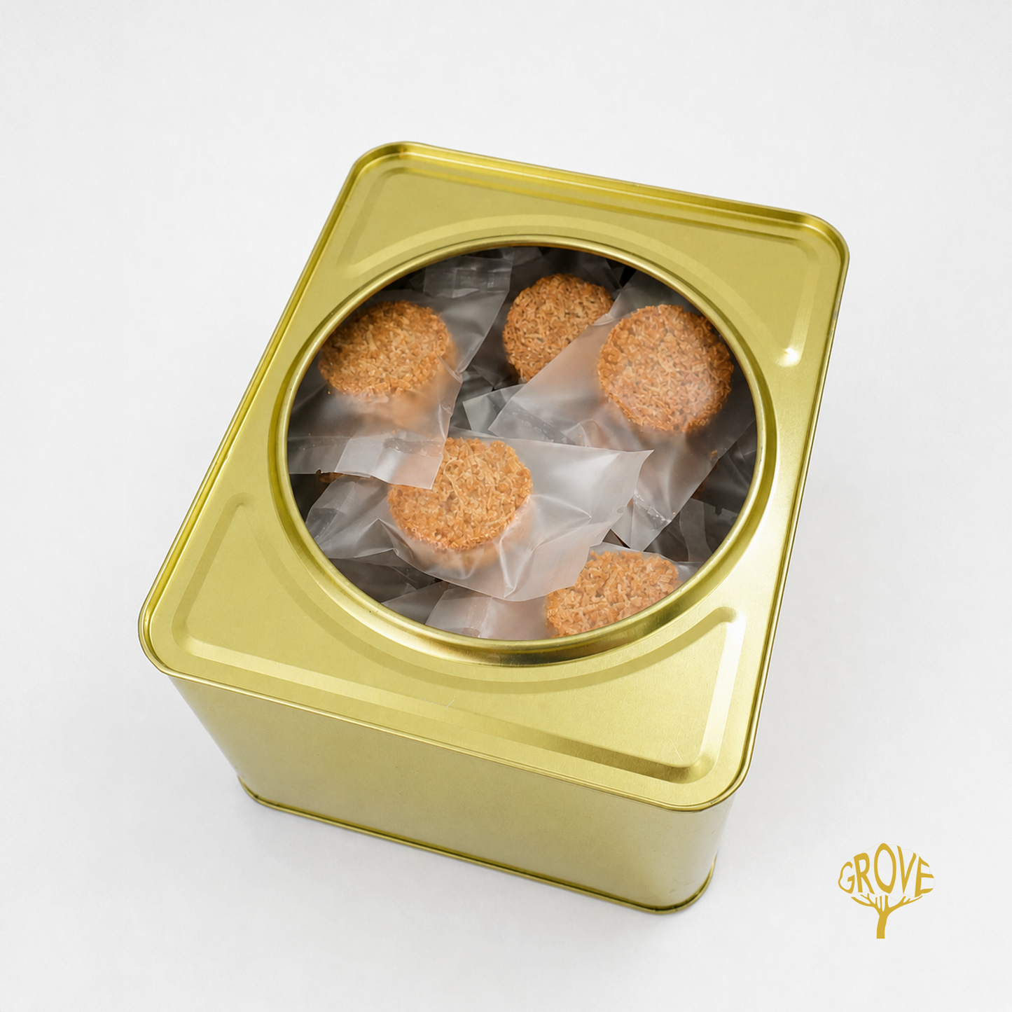 A square gold metal tin with a circular clear window, showing several round brown textured food pieces wrapped in translucent paper inside. A small GROVE logo appears in the bottom right corner on a white background.